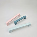 Three pastel-colored cabinet handles on a light gray background