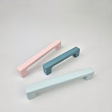 Three pastel-colored cabinet handles on a light gray background