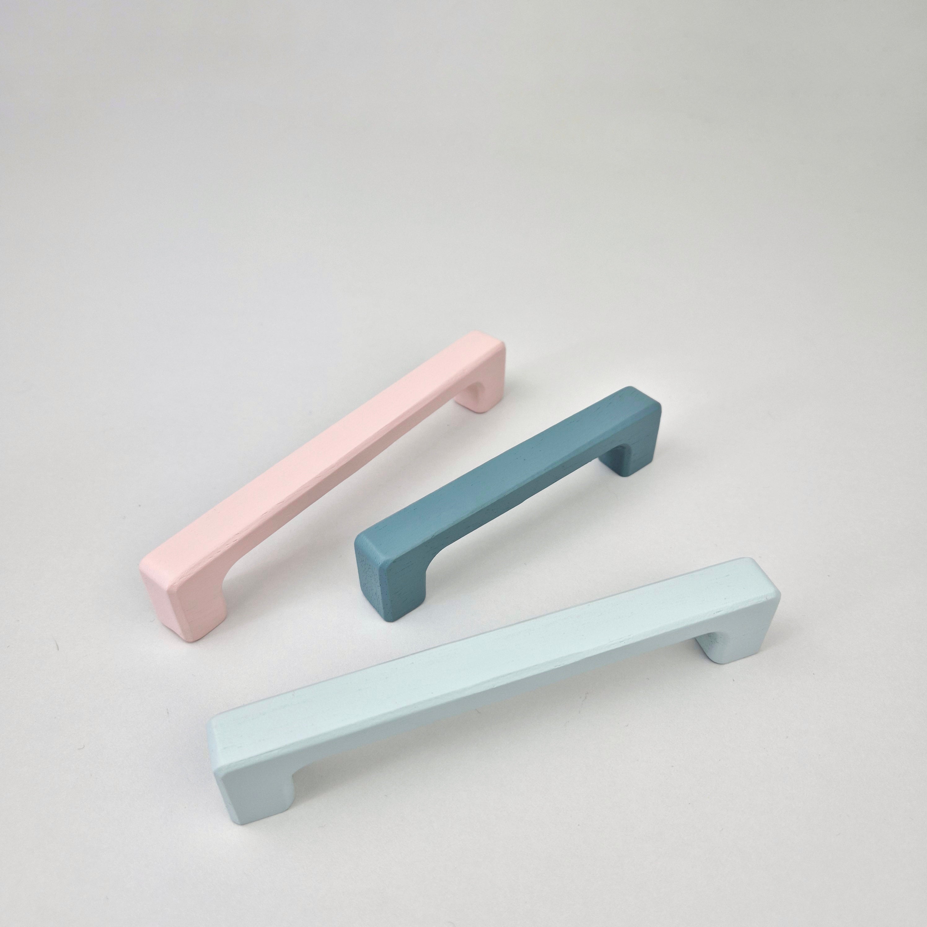 Three pastel-colored cabinet handles on a light gray background