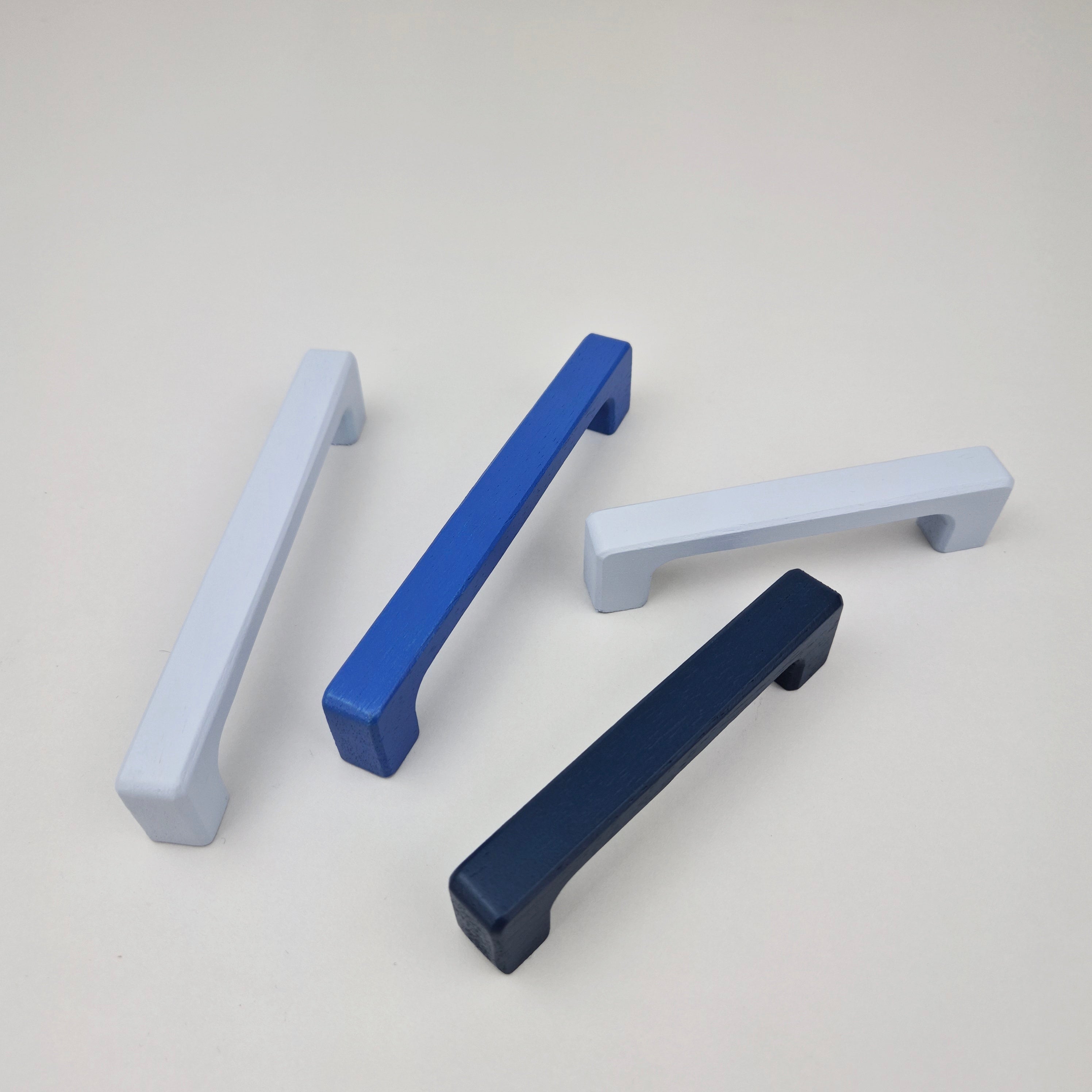 Four cabinet handles in blue, white, and navy on a light gray background