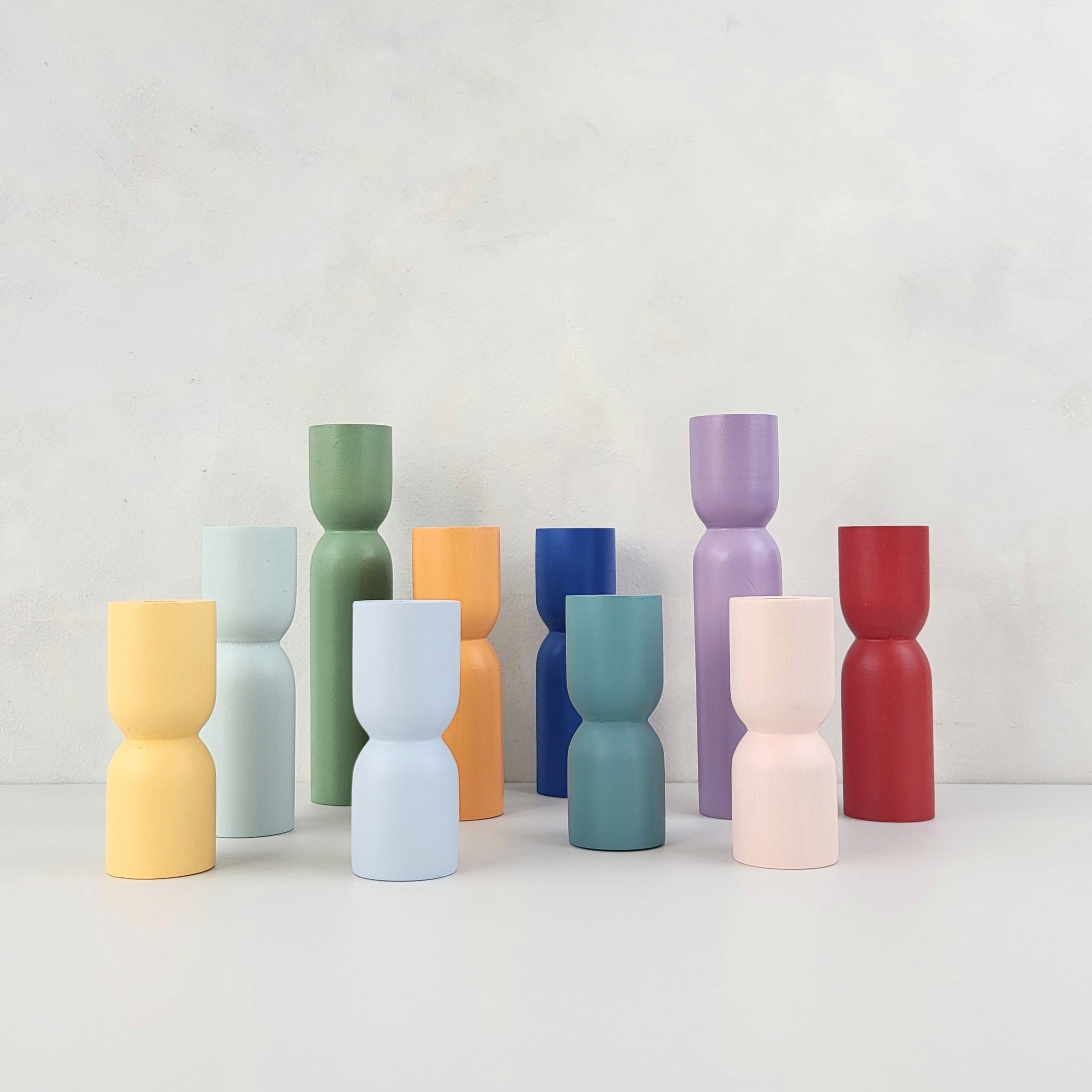 Colorful hourglass shaped vases in various shades of yellow, green, blue, pink, purple, and red arranged on a neutral background.