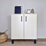 Modern white cabinet featuring dark blue cabinet handles, styled with decorative items and placed on a beige rug.