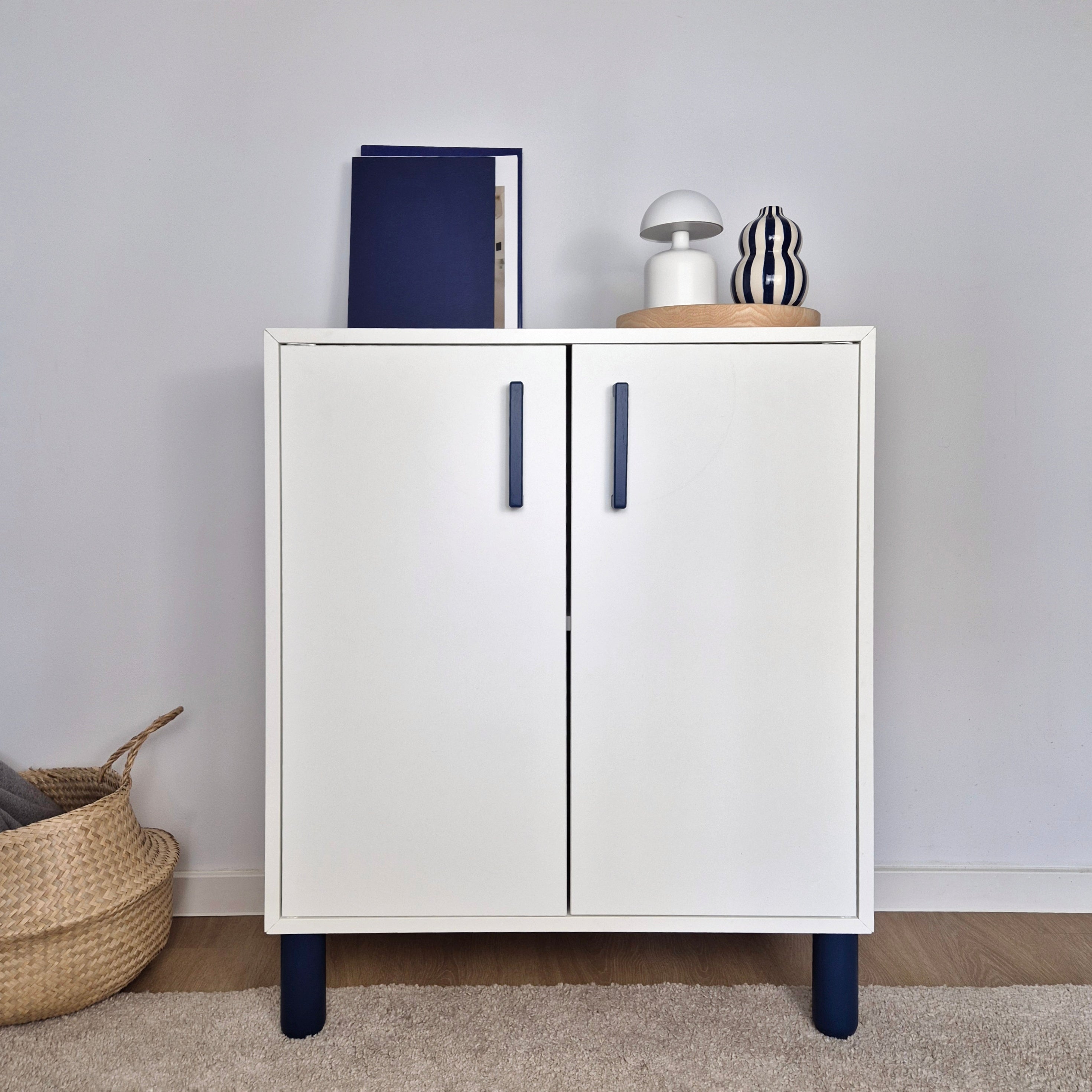 Modern white cabinet featuring dark blue cabinet handles, styled with decorative items and placed on a beige rug.