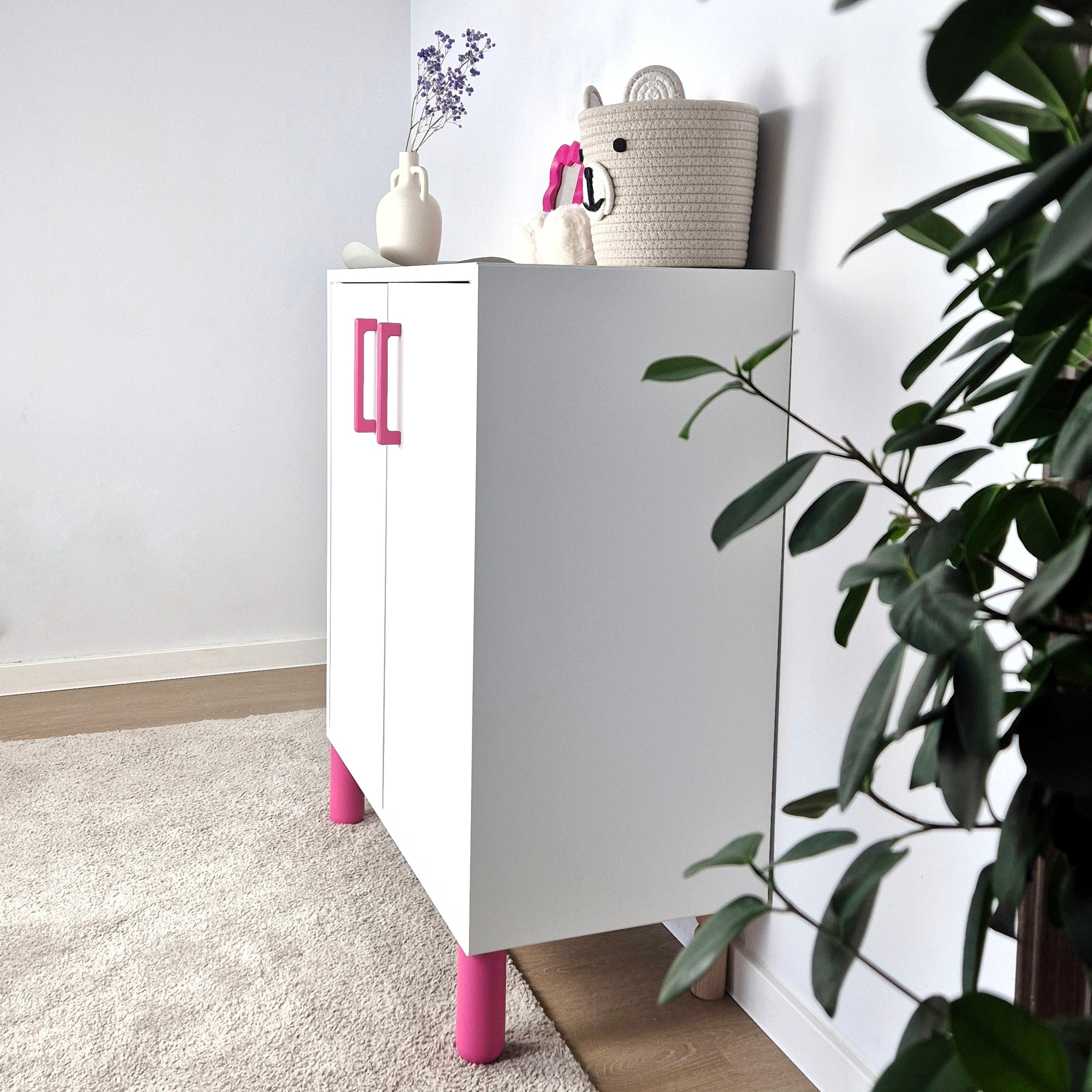 A stylish white cabinet with pink legs, accessorized with decorative items, perfect for kids' room decor. Ball furniture leg.