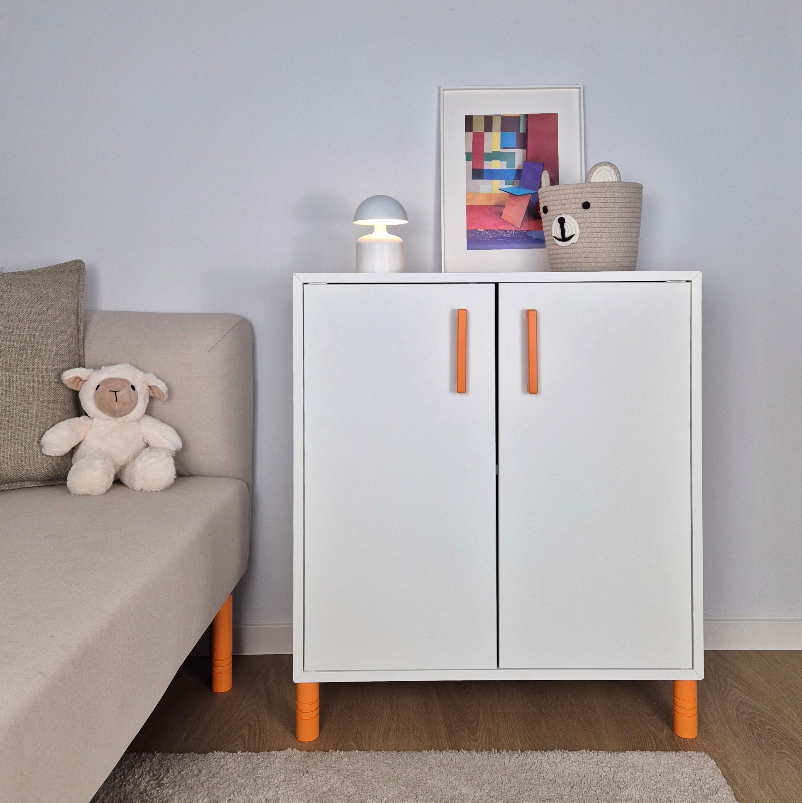 Orange cabinet handle on a stylish white cabinet, adding color to a kids' room decor.