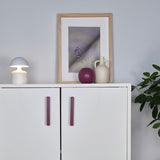White cabinet with purple handles, lamp, and decorative items against a light gray wall.