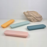 Four rectangular pastel-colored handles on a white surface with a rock in the background.