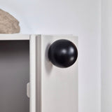 Close-up of a white cabinet with a black knob on a light gray wall.