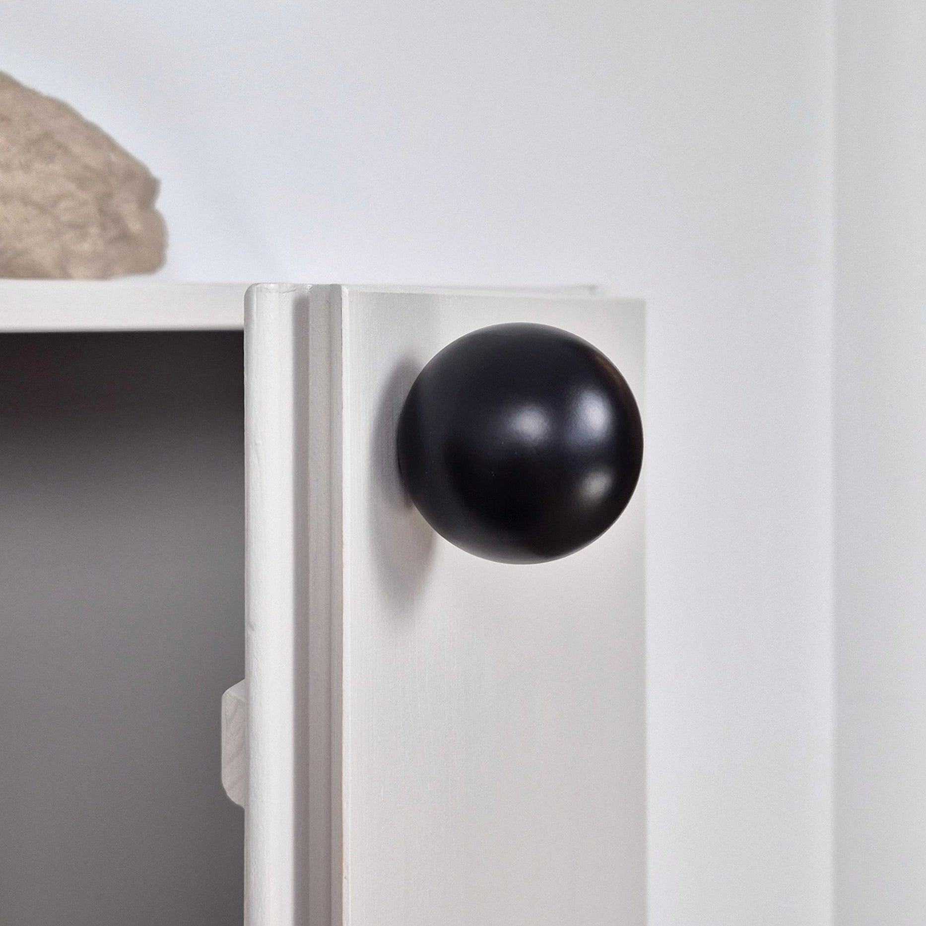 Close-up of a white cabinet with a black knob on a light gray wall.