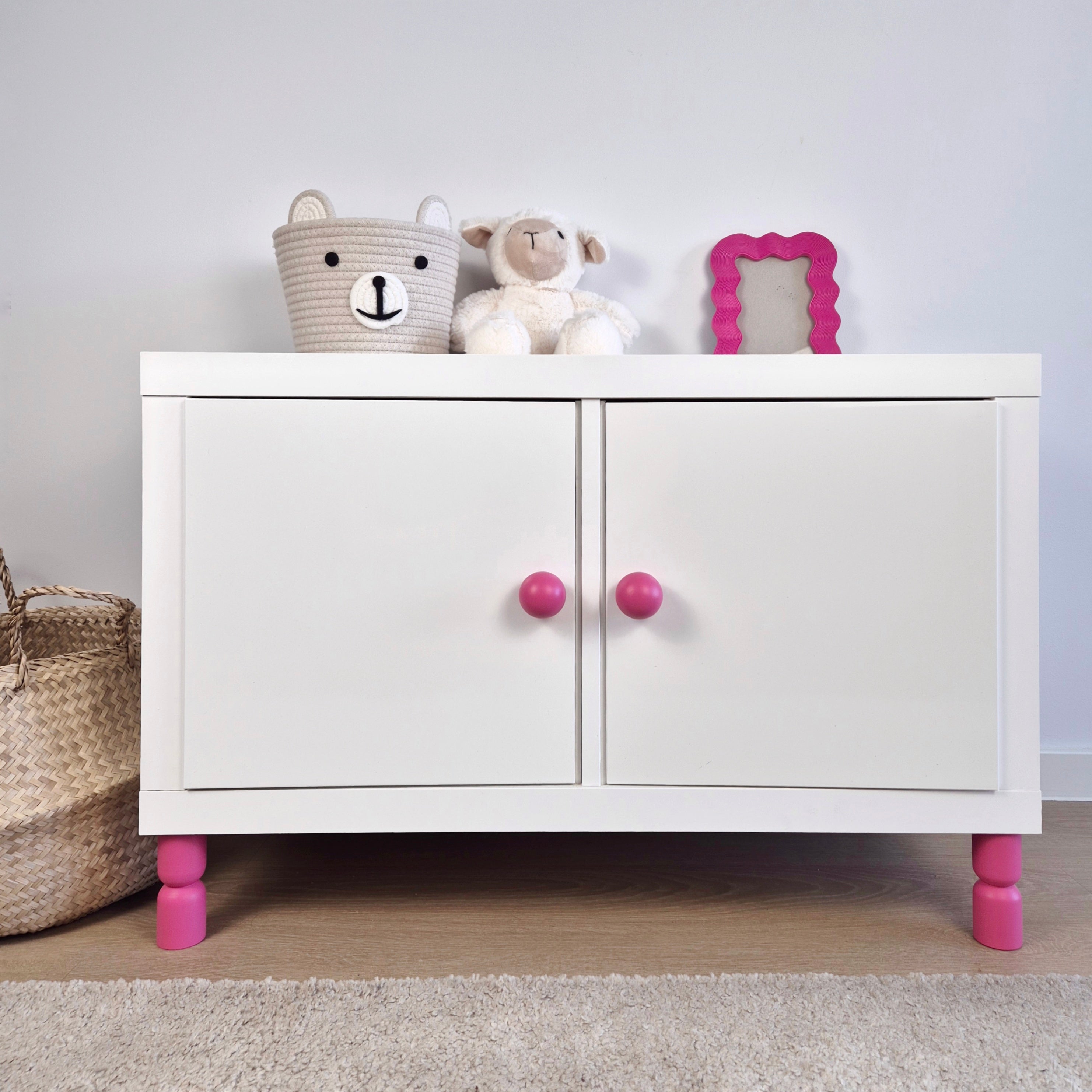 White cabinet with pink furniture legs, stuffed toys, and a decorative frame, showcasing stylish furniture legs.