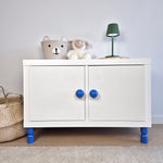 White cabinet with blue furniture legs, stuffed animals, and a lamp, perfect for a child's room.