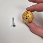Round knob AMBER in hand with a silver screw, showcasing its pressed amber design and round shape.