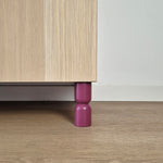 Hourglass shaped furniture legs in purple supporting a bedside table, featuring solid wood design for IKEA furniture.