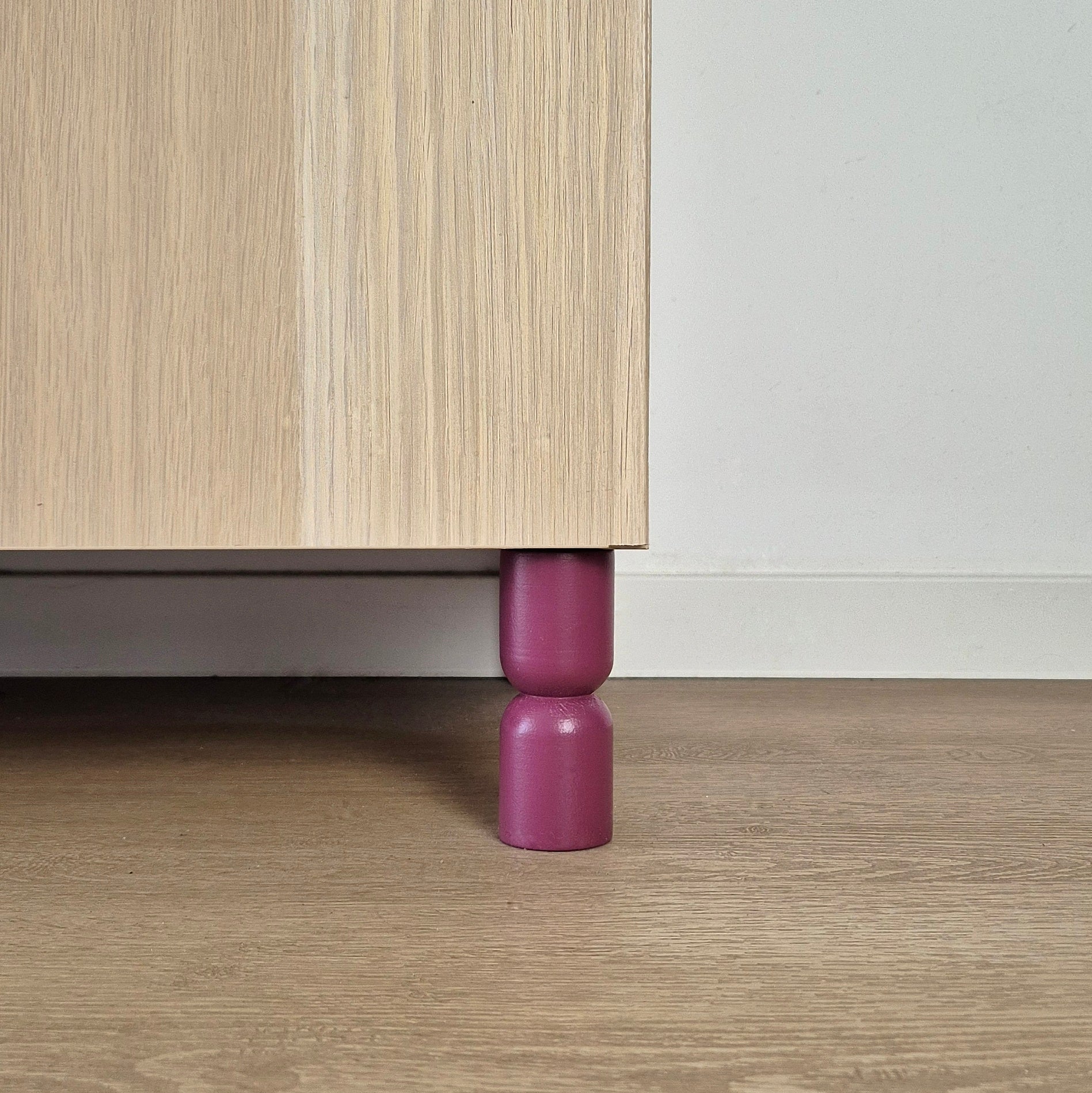 Hourglass shaped furniture legs in purple supporting a bedside table, featuring solid wood design for IKEA furniture.