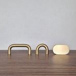 Brass cabinet pull options, including narrow arch, wide arch, and flat oval designs on a wooden surface.