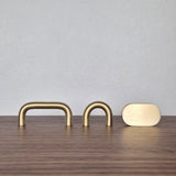 Brass cabinet pull options, including narrow arch, wide arch, and flat oval designs on a wooden surface.
