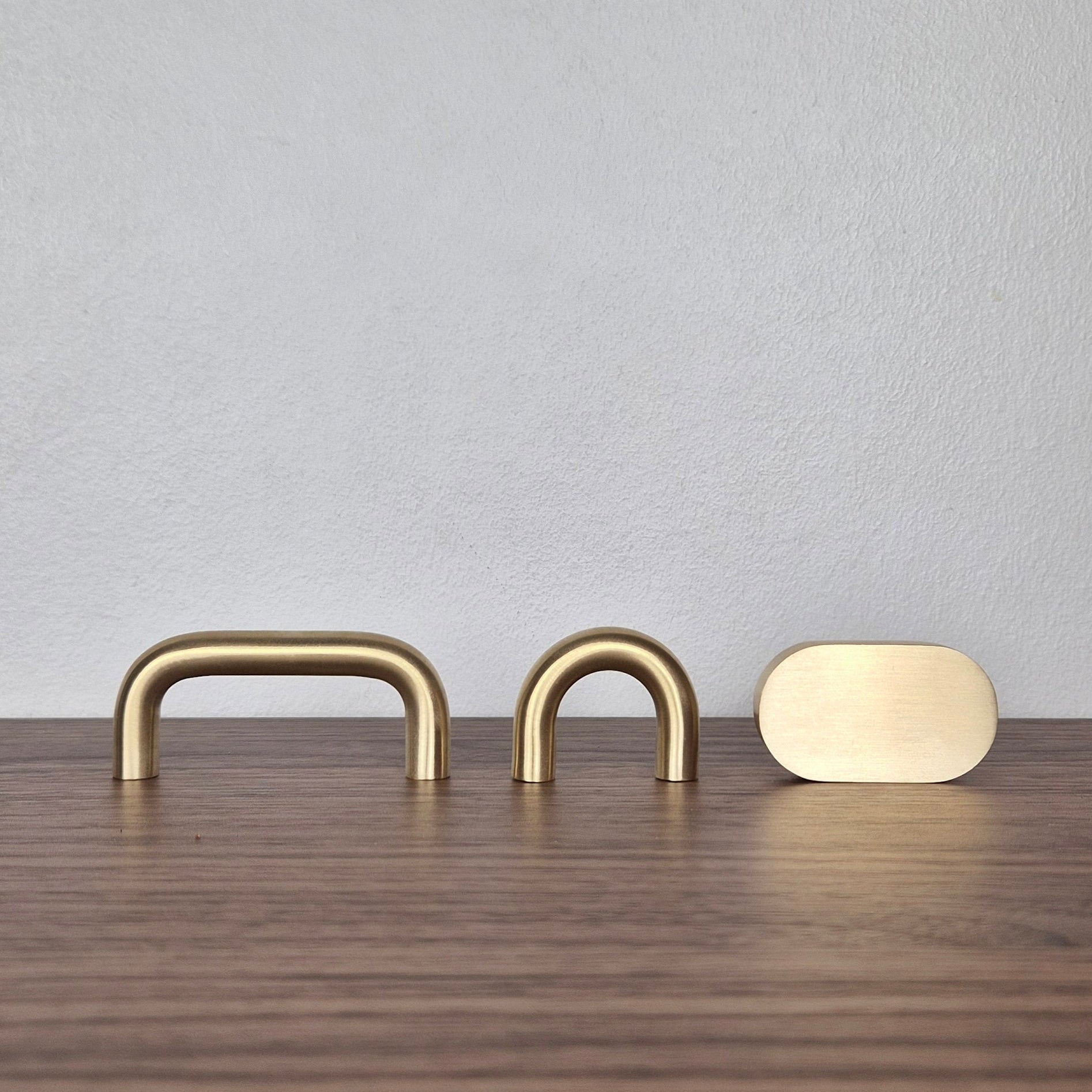 Brass cabinet pull options, including narrow arch, wide arch, and flat oval designs on a wooden surface.