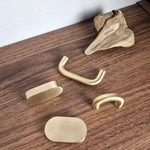 Brass cabinet pull collection on wooden surface, featuring narrow arch, wide arch, and flat oval designs.