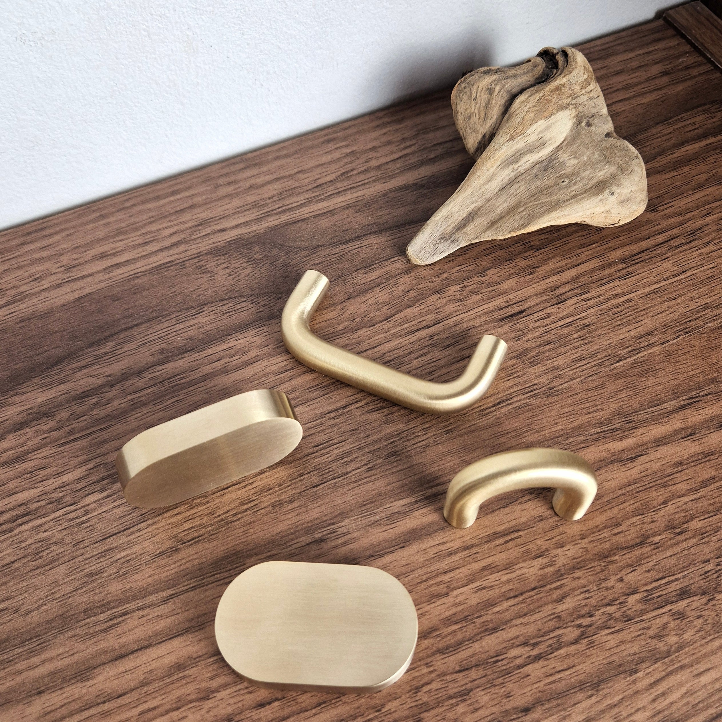Brass cabinet pull collection on wooden surface, featuring narrow arch, wide arch, and flat oval designs.