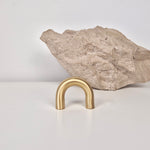 Brass cabinet pull DOME displayed in front of a rock, highlighting its elegant arch design and satin finish.