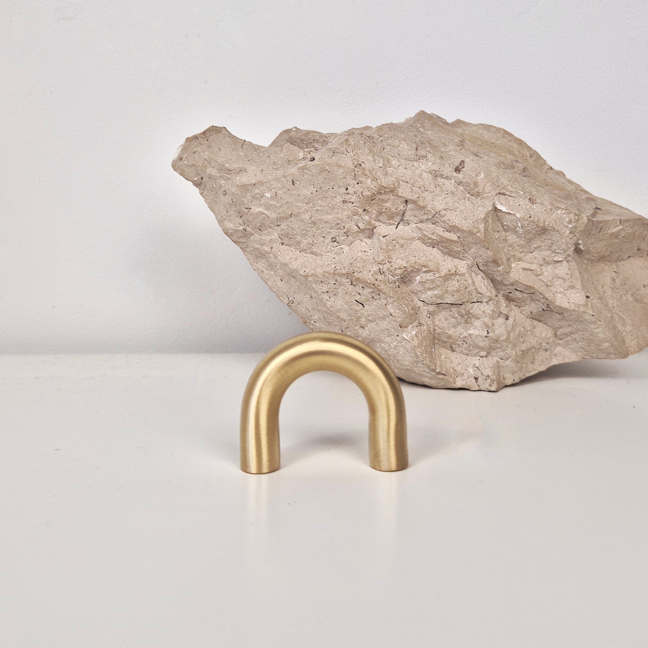 Brass cabinet pull DOME displayed in front of a rock, highlighting its elegant arch design and satin finish.