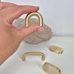 Brass cabinet pull held in hand with various styles displayed on a table against a neutral background.