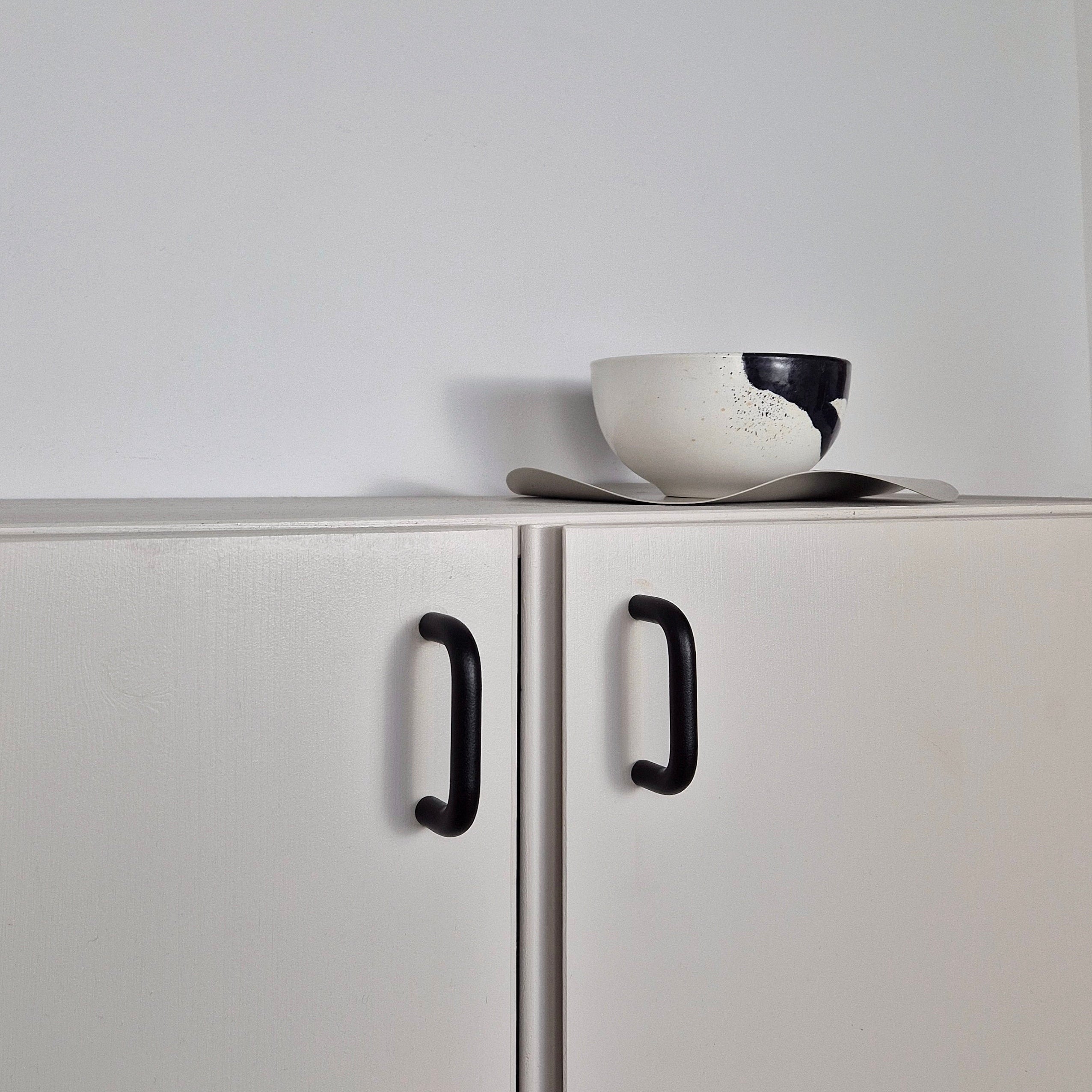 A minimalist white ceramic bowl resting on a white cabinet with black handles.