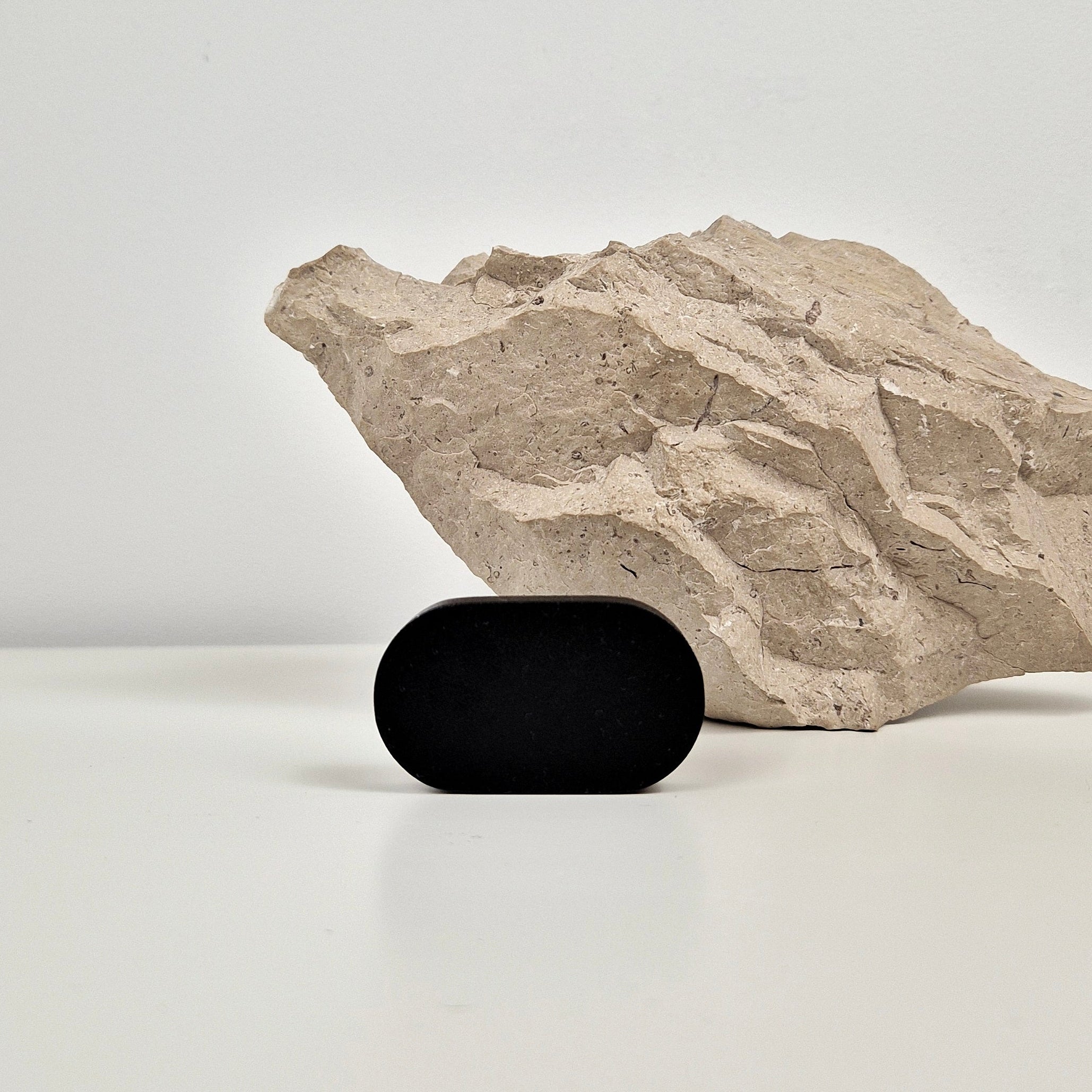 A small matte black oval cabinet knob standing on a white surface in front of a textured beige stone