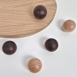 Five round wooden balls in two dark brown and light natural wood finishes are arranged on a white background, with one resting on a curved wooden board.