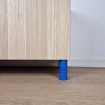 Striped blue ball furniture leg supporting a wooden cabinet on a light floor.
