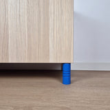 Striped blue ball furniture leg supporting a wooden cabinet on a light floor.