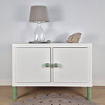 White cabinet with green Ball furniture legs, a lamp on top, and decorative stone, enhancing modern interior decor.