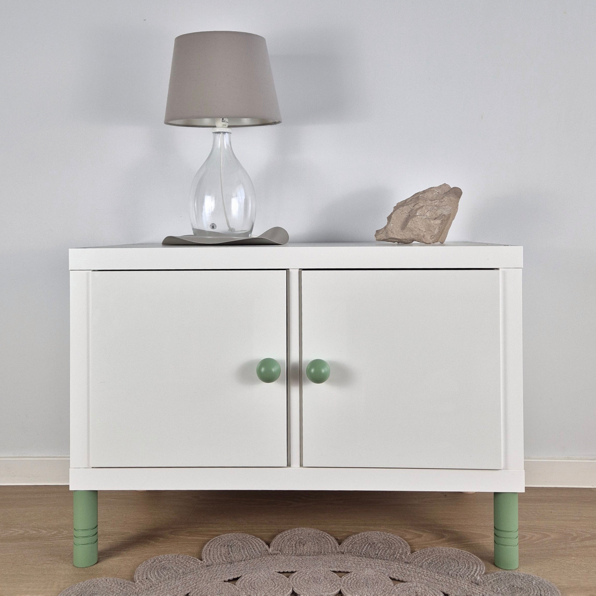 White cabinet with green Ball furniture legs, a lamp on top, and decorative stone, enhancing modern interior decor.