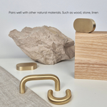 Brass cabinet pull displayed with natural materials like wood and stone, showcasing its elegant design and finish.