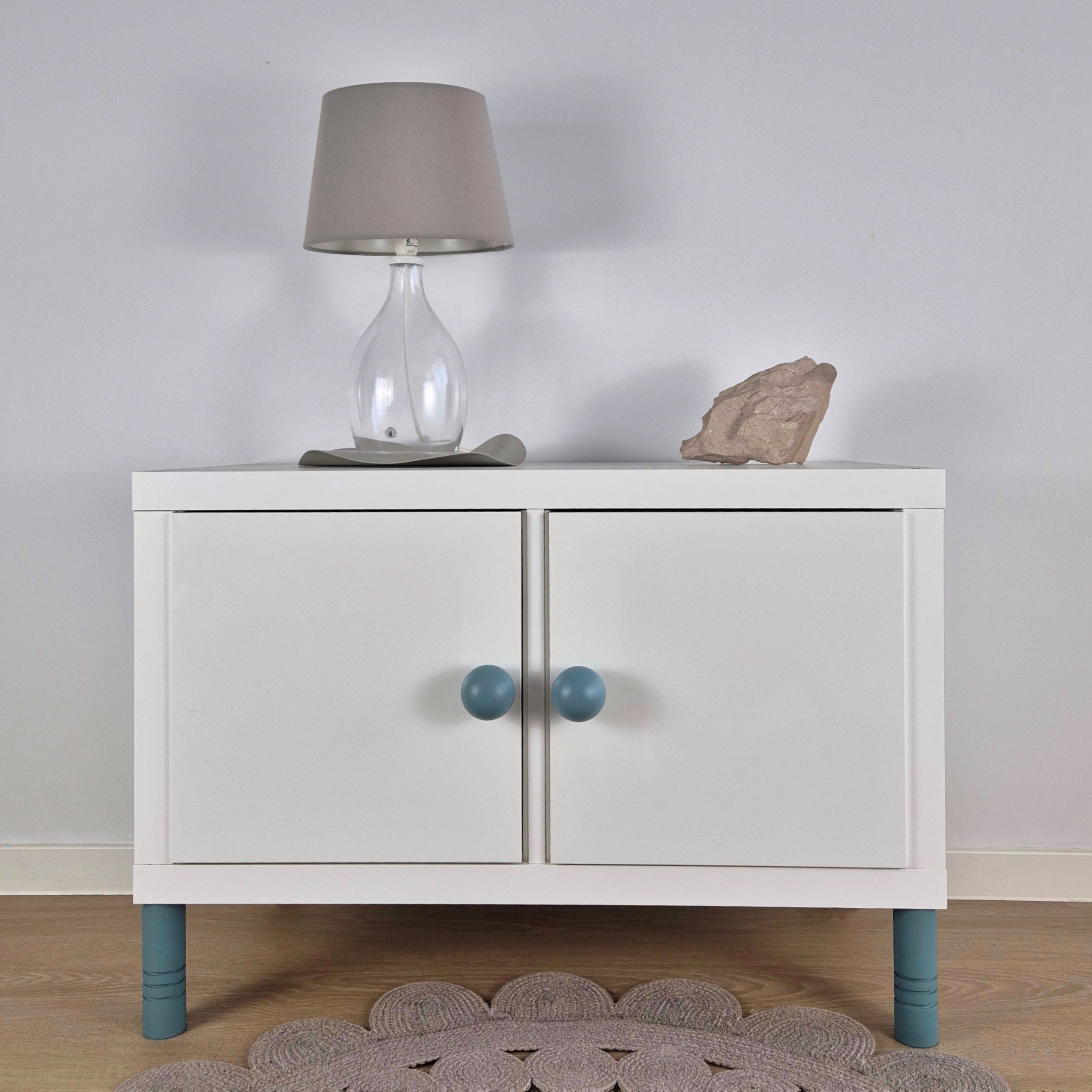 View of a stylish bedside table with striped furniture legs, a lamp, and decorative stone on top.