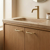 Brass cabinet pull on a modern wooden bathroom cabinet with a stone countertop and faucet.