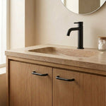 A modern bathroom vanity featuring a warm beige stone countertop with an integrated sink, a matte black faucet, and light oak wood cabinet doors with black handles.
