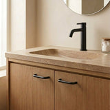 A modern bathroom vanity featuring a warm beige stone countertop with an integrated sink, a matte black faucet, and light oak wood cabinet doors with black handles.