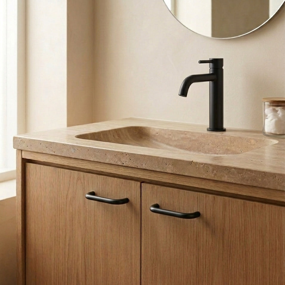 A modern bathroom vanity featuring a warm beige stone countertop with an integrated sink, a matte black faucet, and light oak wood cabinet doors with black handles.